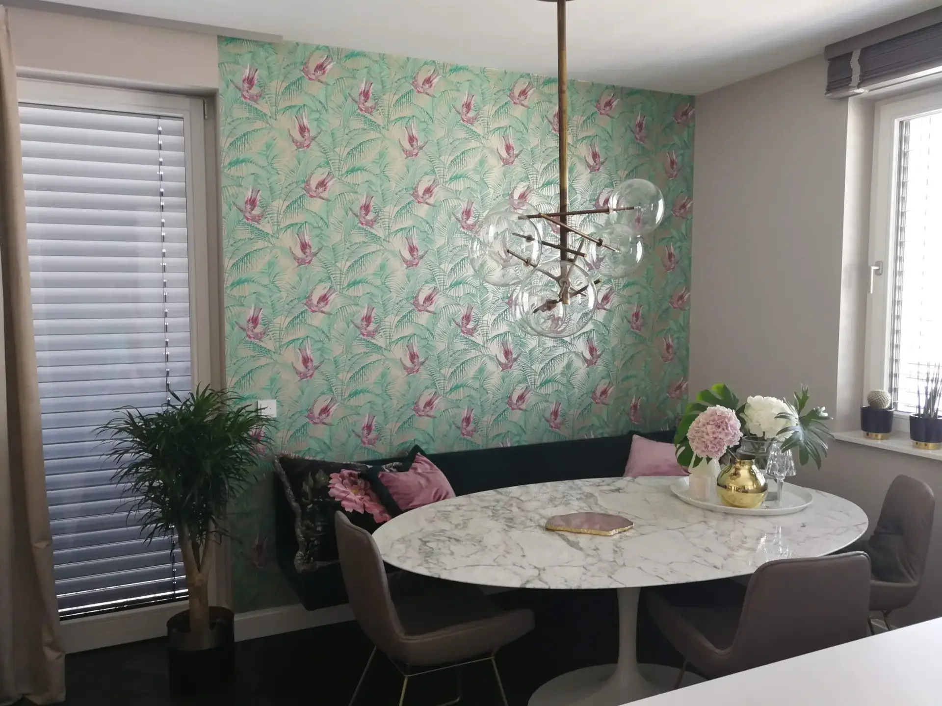 Eine hochwertige Designertapete mit einem detailreichen Muster aus tropischen Vögeln und Palmwedeln in Türkis und Rosa, professionell an der Akzentwand eines stilvollen Essbereichs angebracht.
