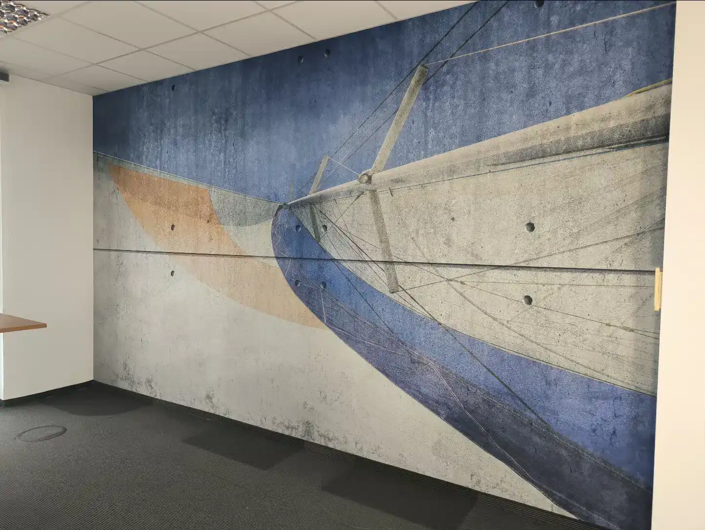 Großflächige Fototapete mit abstraktem Segelschiff-Motiv auf einer Wand in Betonoptik in einem modernen Büroraum.