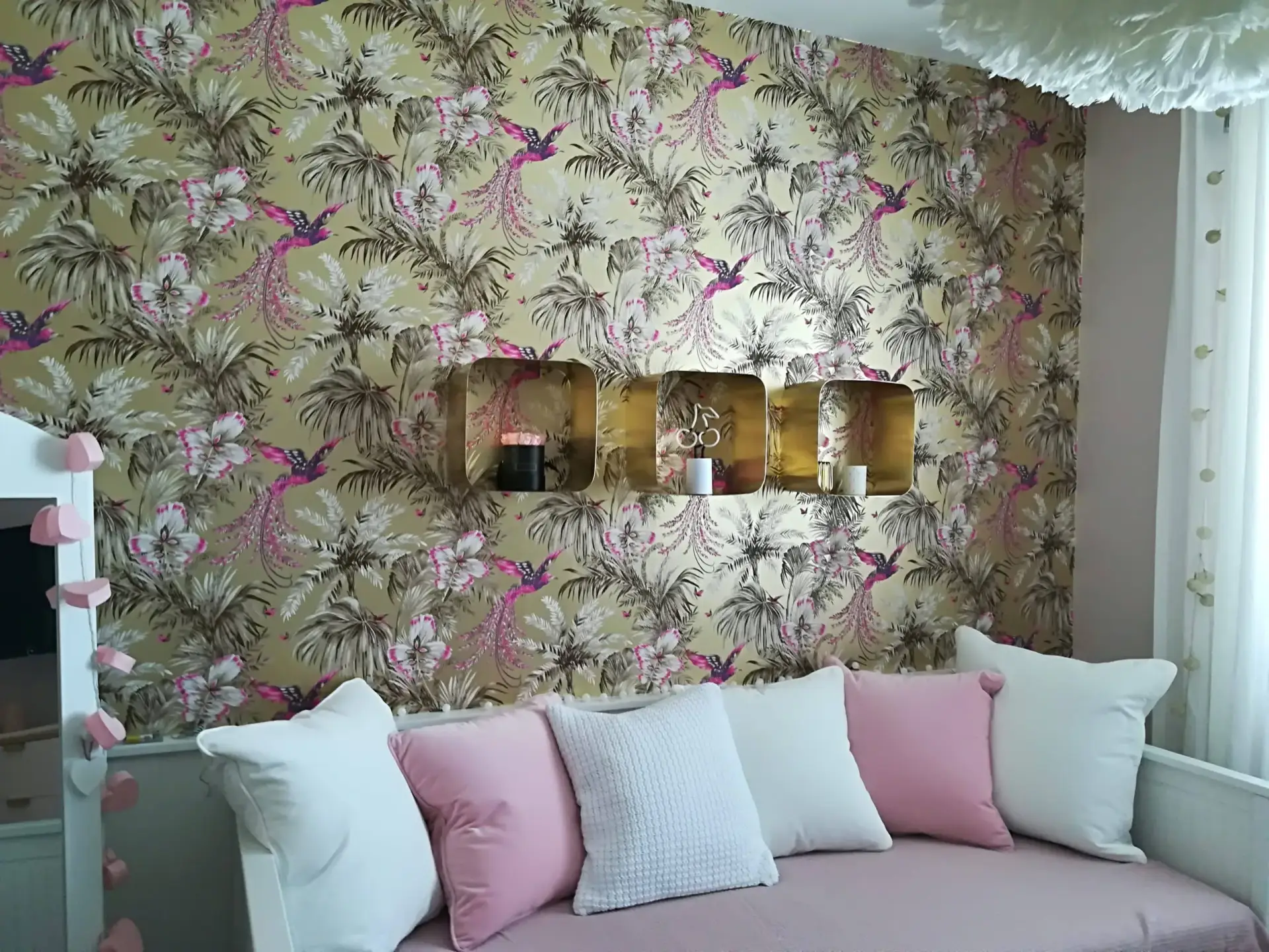 Detailreiche Wandgestaltung im Wohnzimmer mit einer hochwertigen Motivtapete (pinke Vögel und Palmenblätter auf goldenem Grund).