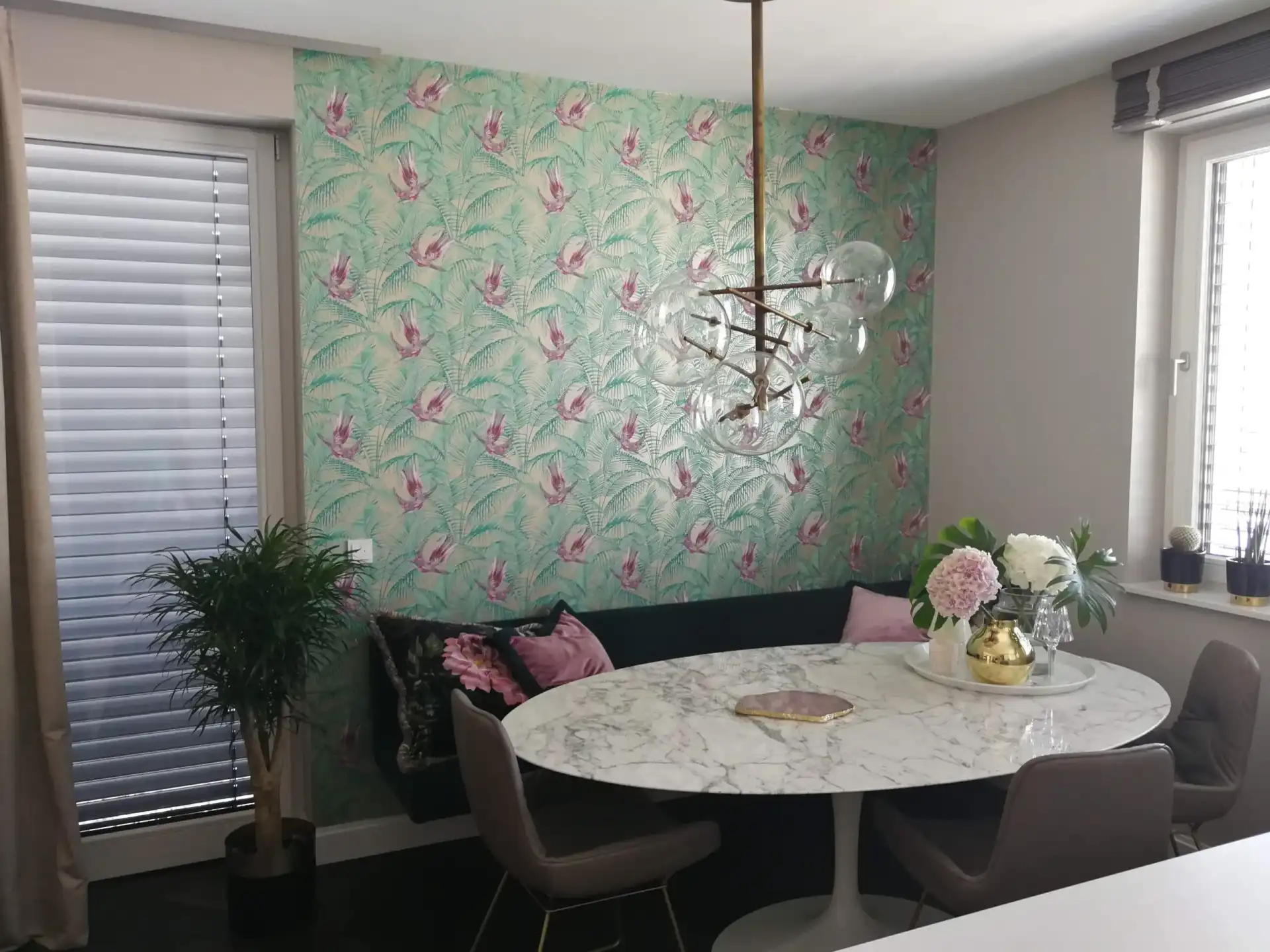 Eine hochwertige Designertapete mit einem detailreichen Muster aus tropischen Vögeln und Palmwedeln in Türkis und Rosa, professionell an der Akzentwand eines stilvollen Essbereichs angebracht.